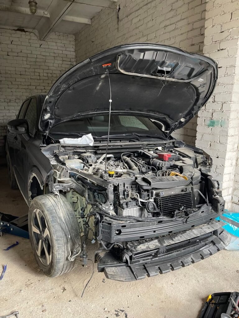 Juodas daužtas automobilis po eismo įvykio su atidarytu kapotu paruoštas supirkimui.