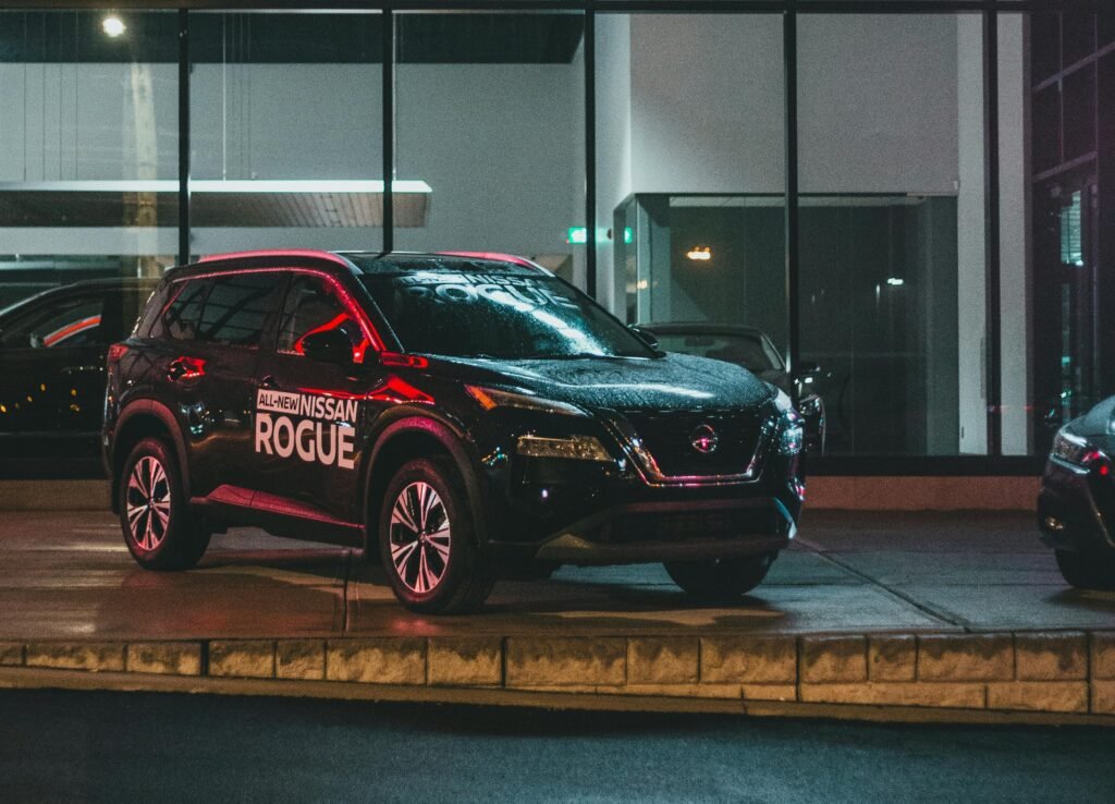 uodas visureigis "All-New Nissan Rogue" naktį, apšviestas raudona šviesa, stovintis prie automobilių salono vitrinos. Matomas užrašas "ALL-NEW NISSAN ROGUE".