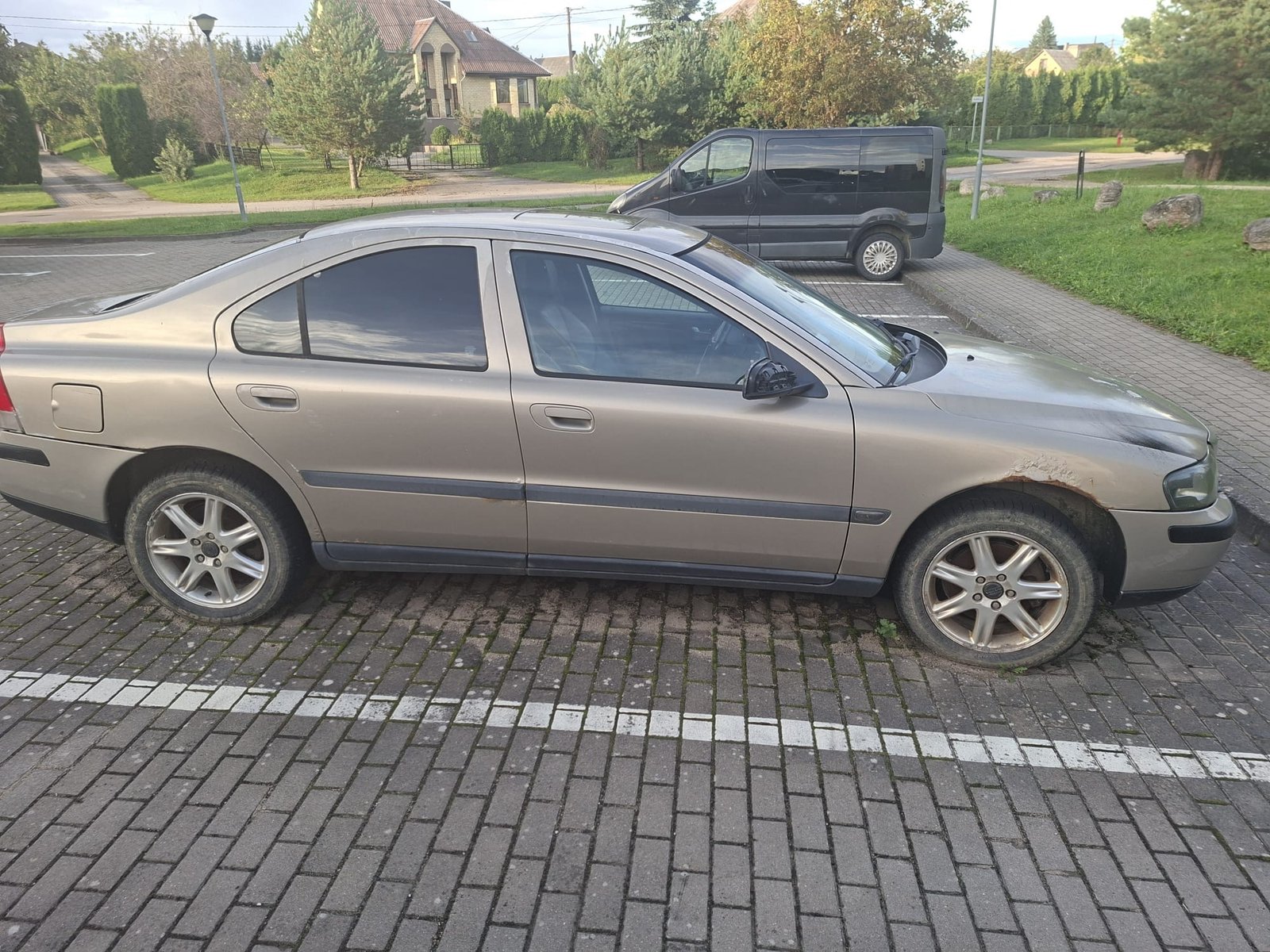 Senas pilkas sedanas su ryškiais rūdžių pažeidimais ant galinio sparno. Pavyzdys seno automobilio su kėbulo defektais, kurį galima parduoti.
